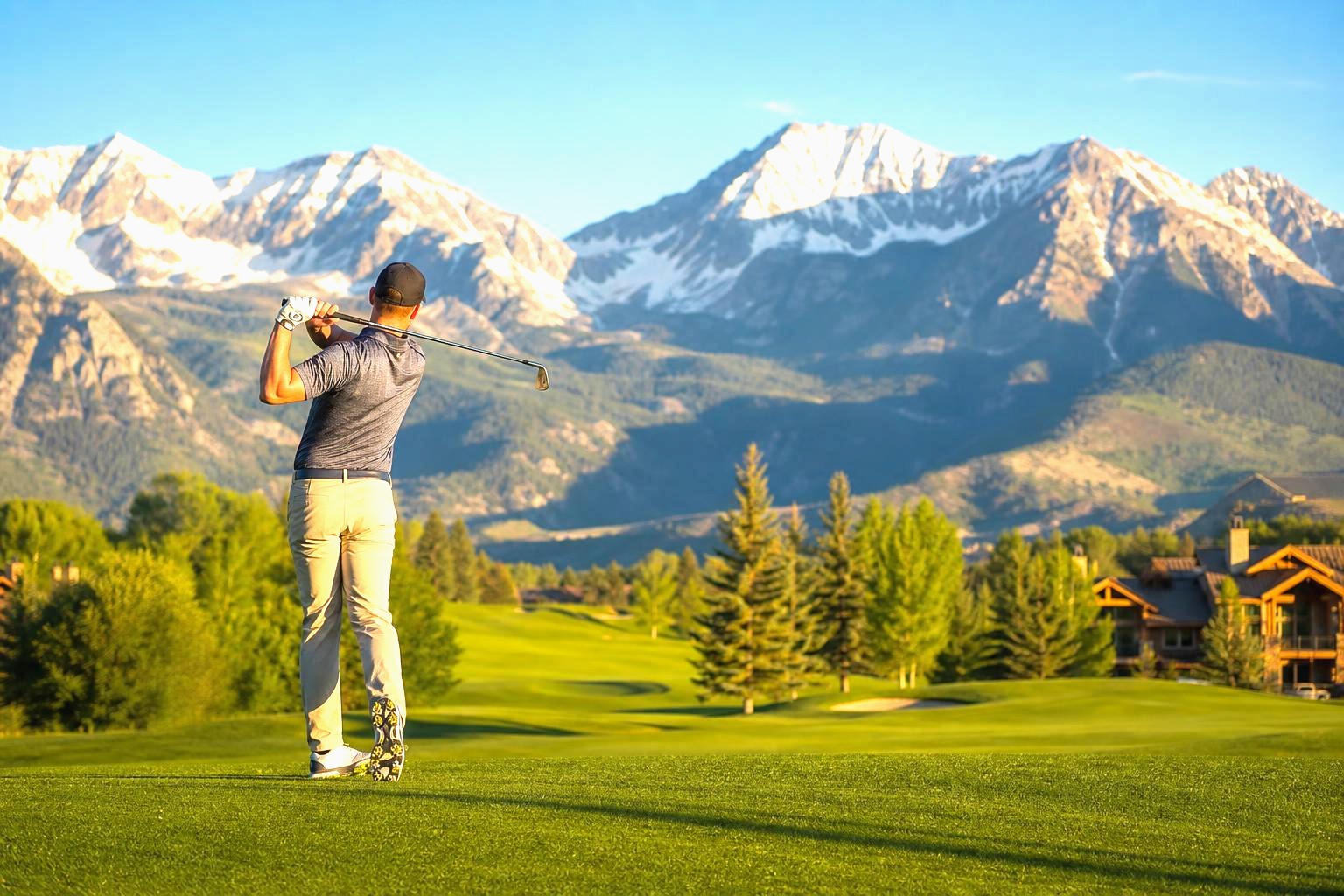 Golfer driving on a bright Colorado mountain fairway with the snow-capped Rockies behind